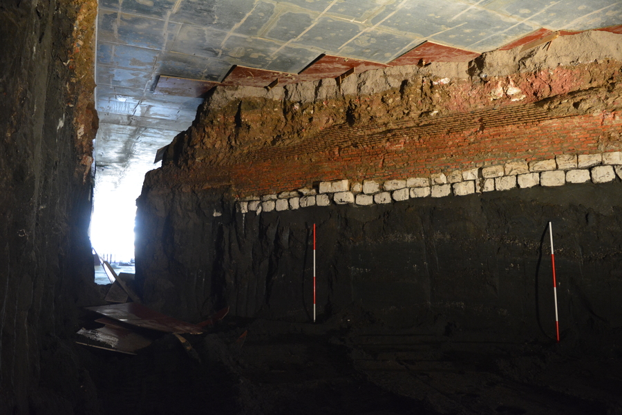 Zicht op de buitenzijde van de muur. Van onder naar boven de natuurlijke geologische lagen, het fundament uit krijtsteen en de bakstenen voet.